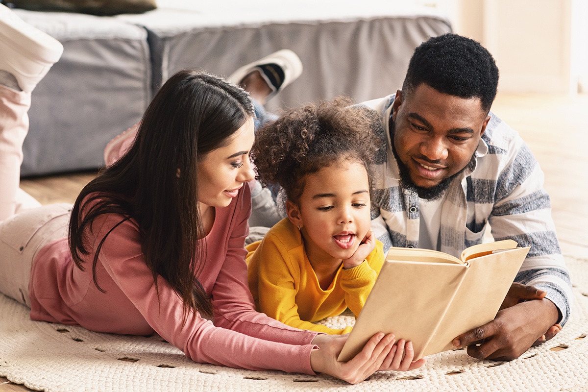 Rodzic czyta kolorową książkę małemu dziecku siedzącemu na kolanach w przytulnym pokoju