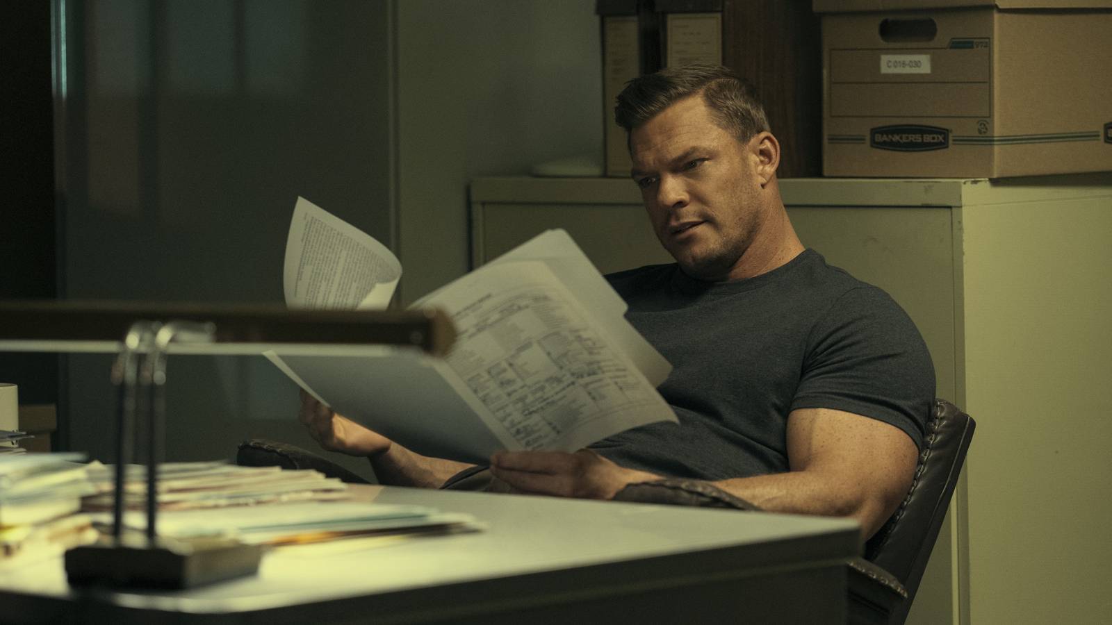 Pracownik biurowy czyta książkę przy biurku z laptopem kubkiem kawy i stertą dokumentów